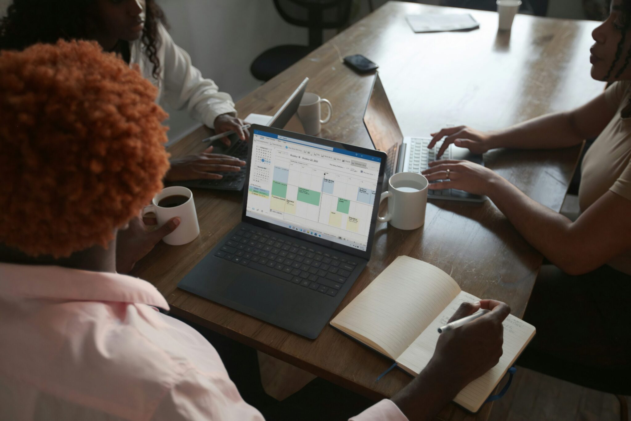 Introducing-the-New-Microsoft-Planner-Everything-You-Need-to-Know--scaledjpg | ALCON DTS: Austin, TX Best Managed IT Support Services Three people in a meeting at a table discussing schedule on their Microsoft laptop